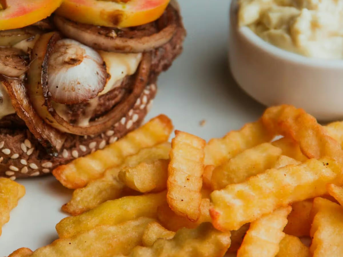 Kroepoekfrites en een bakje saus naast een burger met gebakken ui.